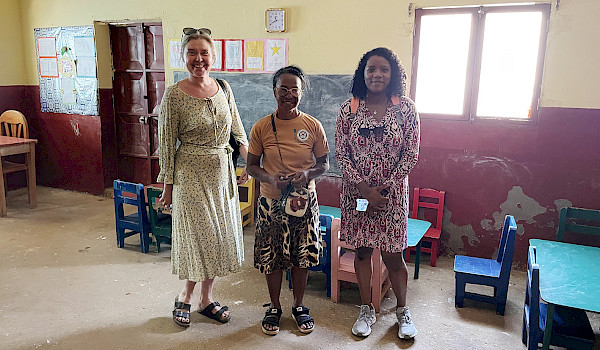 De tre står og smiler i kameraet i et klasserom for små barn.
