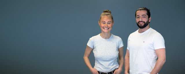 Jente med lyst hår i topp og gutt med skjegg smiler mens de ser rett i kamera
