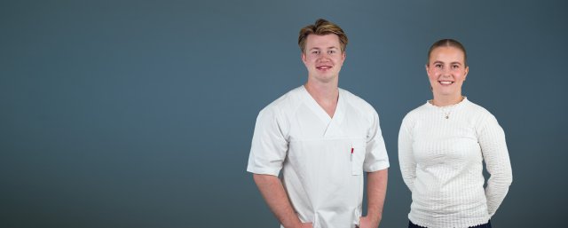Gutt i sykepleieruniform og jente i hvit genser ser i kamera og smiler.