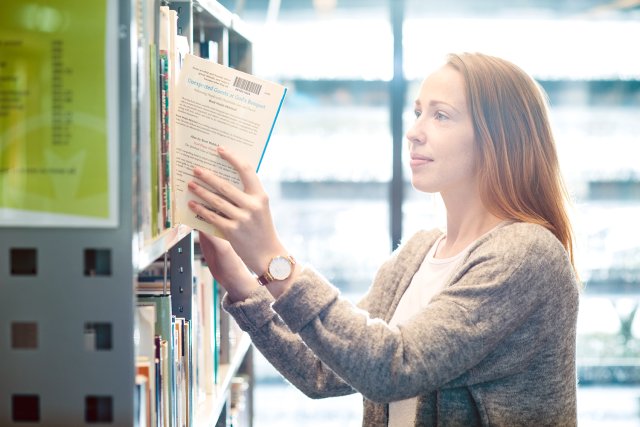 Jente tar en bok ut av en bokhylle