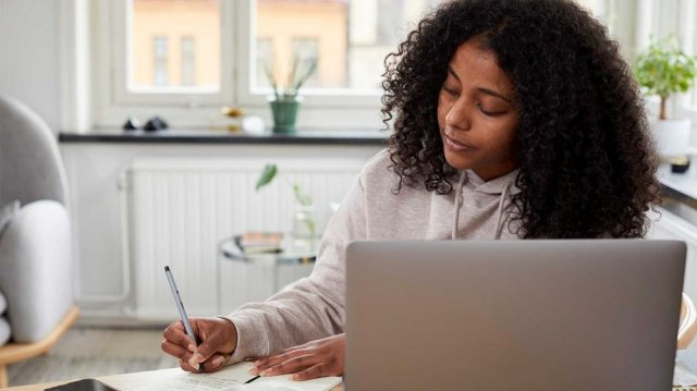 Ung kvinne noterer i en notatblokk ved siden av en laptop