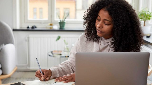 Ung kvinne har en pc foran seg og skriver i en notatbok
