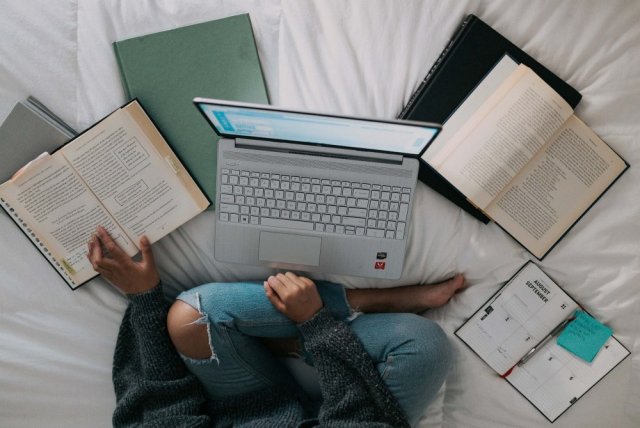 En laptop i en seng med flere åpne bøker rundt seg