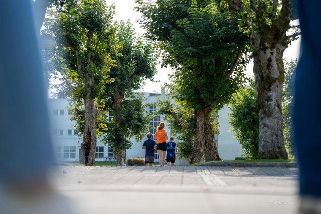 Tre mennesker løper mellom to rekker med trær