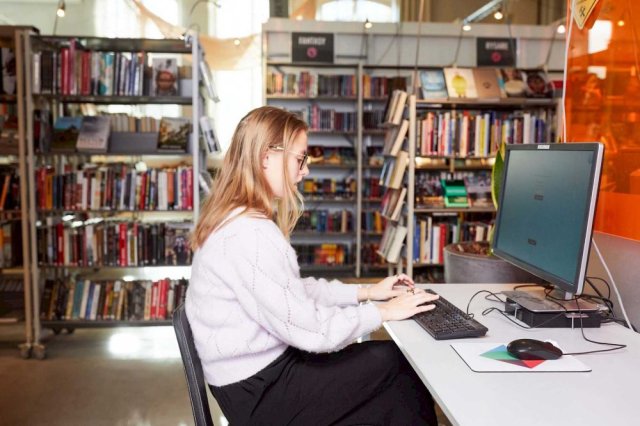 Kvinne sitter på et bibliotek og taster på en pc