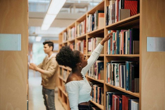 Kvinne plukker ut bok i en bibliotekshylle
