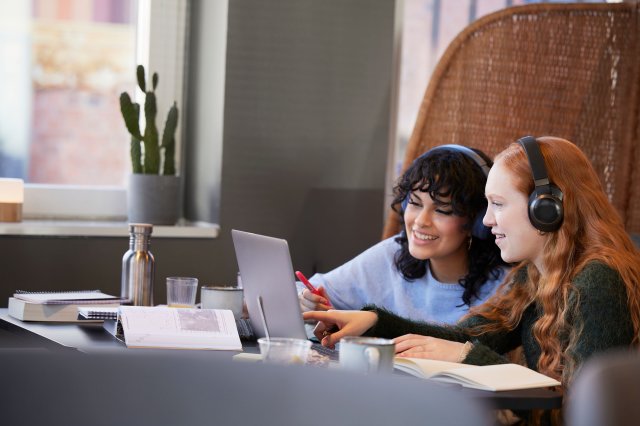 To unge kvinner sitter ved en pult og arbeider på en laptop