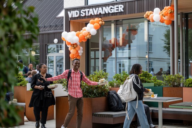 Glade studenter utenfor hovedinngangen på campus