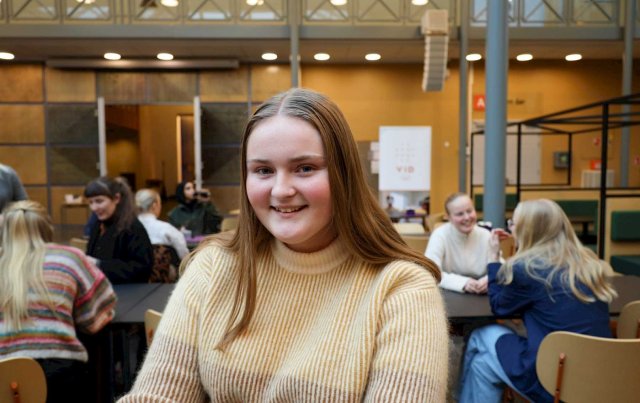 Portrett av Kathrine tatt i atriet ved VID. Studenter i bakgrunnen.
