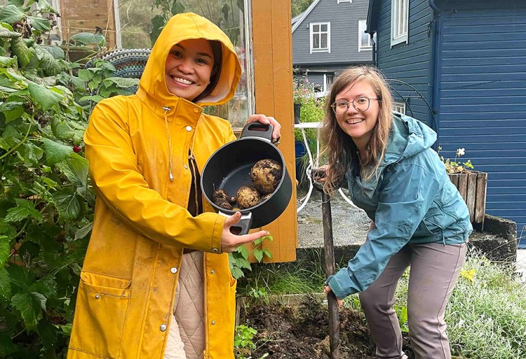  bilde av to jenter i grønnsaksåker som holder opp en kjele med poteter