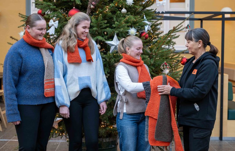 Britha og to studenter til overrekker strikkede skjerf til representant for Kirkens bymisjon