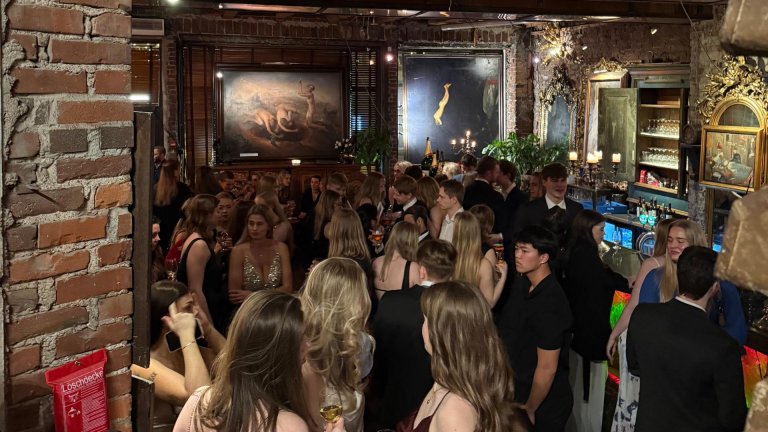 En stor gruppe mennesker er samlet i et selskapslokale iført selskapsklær