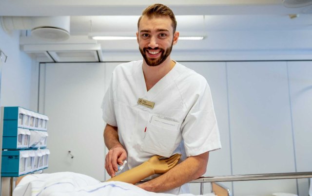 Ung mann i sykepleieruniform smiler til kamera