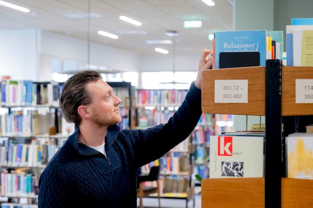 A student picking a book from a shelf in the library on the Stavanger campus.