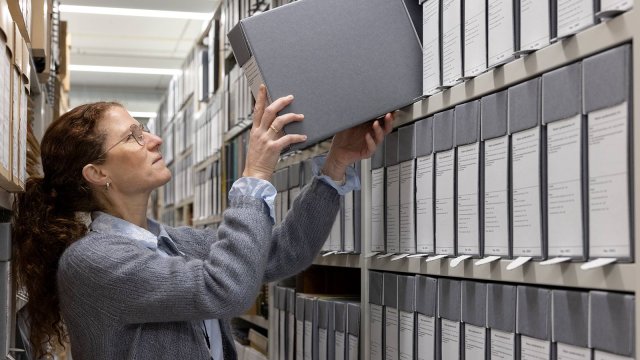 En dame setter en eske inn i en arkivhylle