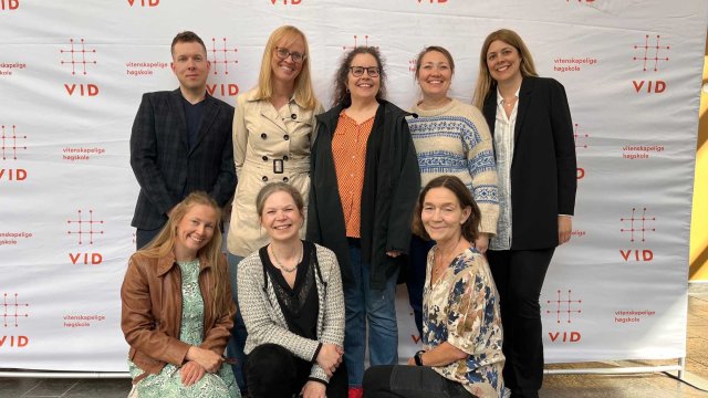 Eight people in front of the VID photo wall