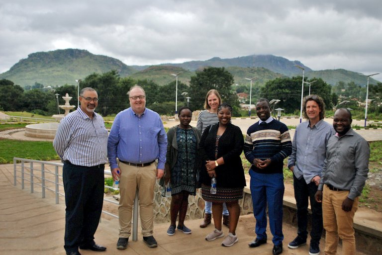 Group photo of men and women. In the background you can see green hills.