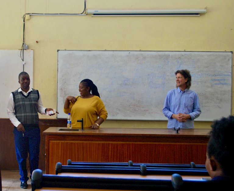 Two men and a women in front of a backboard in a classroom in Malawi
