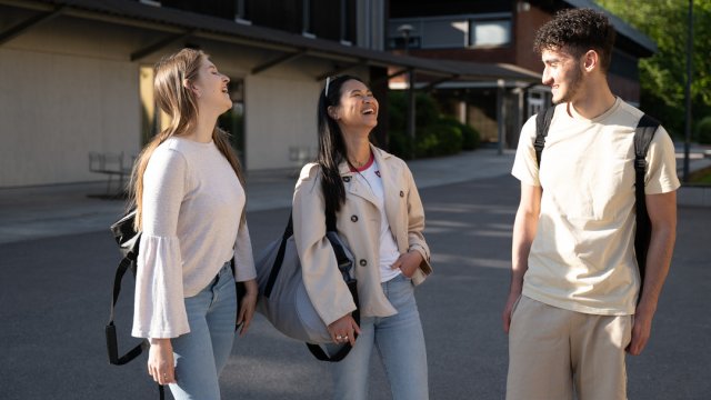 Tre studenter står ute og smiler