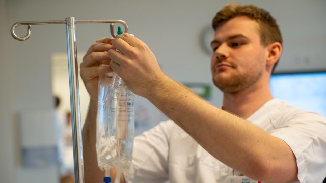 En mannlig sykepleier henger opp en pose med intravenøs væske på et stativ