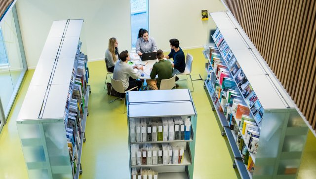 Studenter sitter rundt et bord i et bibliotek