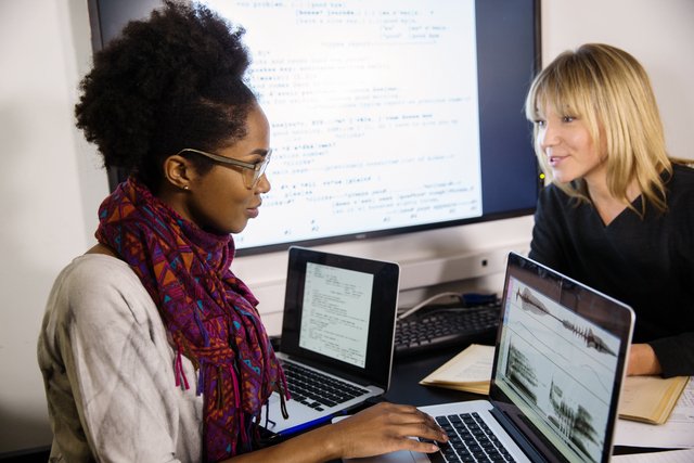 To damer sitter ved et bord og skriver på en laptop
