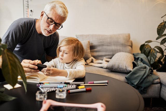 Mann og et lite barn samhandler ved et bord hvor det ligger skriveblokk og tusjer