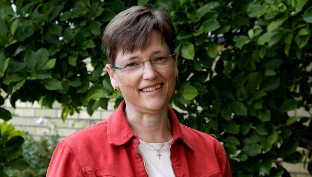 Dame med briller og rød jakke står foran en busk