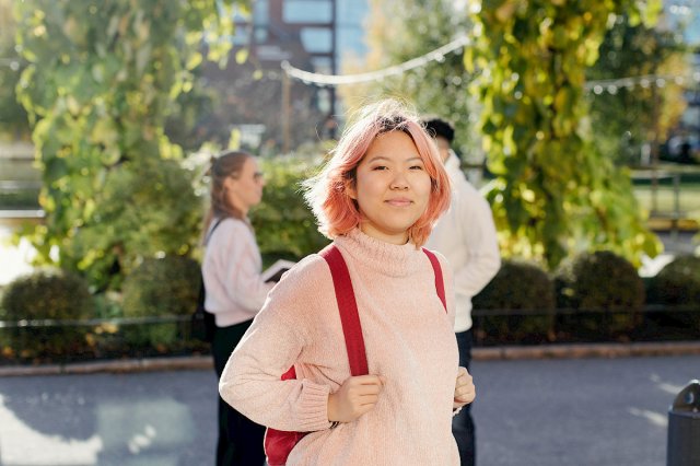 En jente med rosa hår og skolesekk ser i kamera