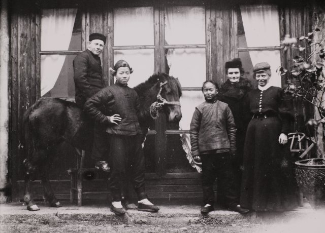Karl Ludvig Reichelt og konen Anna Kristine og Marie Nilsen sammen med hestepasserne An Fuh og An Chao utenfor misjonsstasjonen i Ningxiang.
