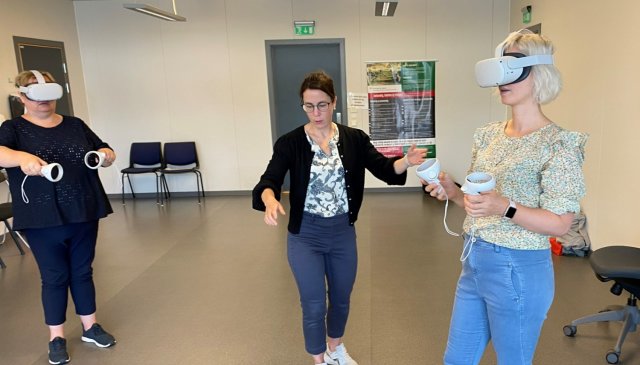 To personer står med VR-briller mens en instruktør hjelper.