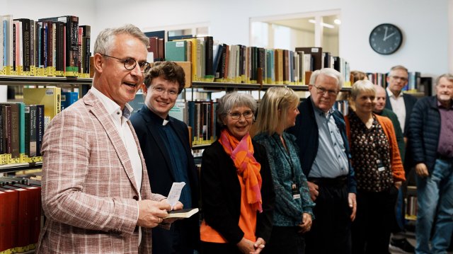 Bård Mæland står i biblioteket og snakker. En rekke tilhørere står ved siden av han.