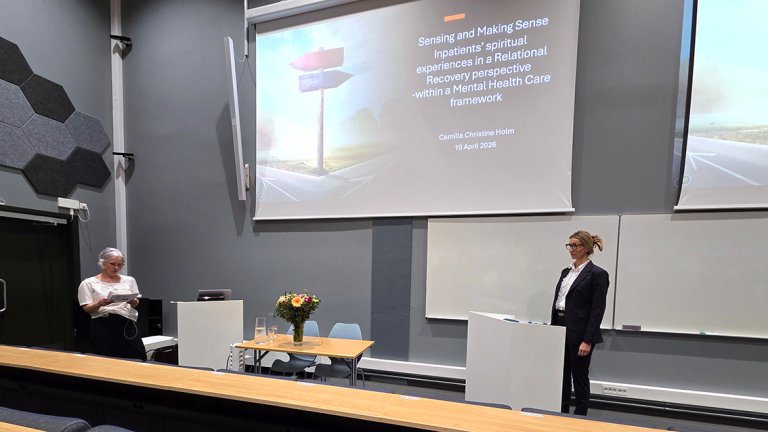 Camilla Holm står og snakker foran powerpoint. 