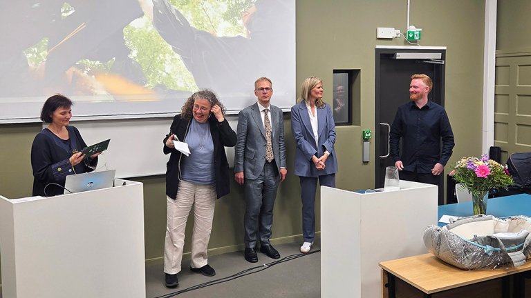 bilde av fem personer foran powerpoint i forelesningssal. 