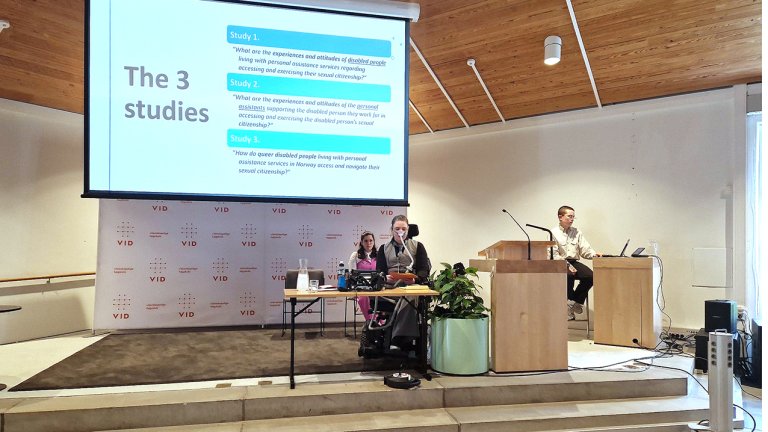 Thunem og to andre sitter forrest i forelesningssal foran powerpoint. 