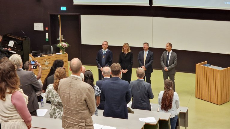 bilde tatt fra bak i forelesningssal. Man ser ryggen på publikum og Dag-Håkon med veiledere og disputasledere foran på scenen.