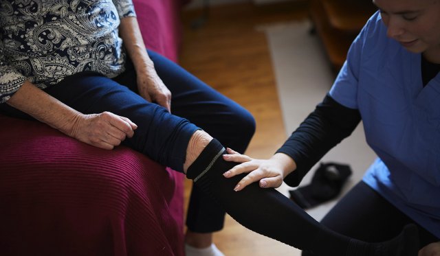 En eldre kvinne får hjelp med støttestrømpene av helsepersonell.