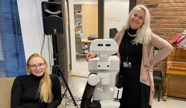 Personene står med en robot mellom seg
