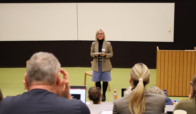 Kristin står i forelesningssal og snakker, man ser bakhodet på publikum