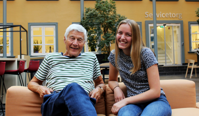 En mann og en ung jente sitter på en sofa. De ser i kameraet og smiler.