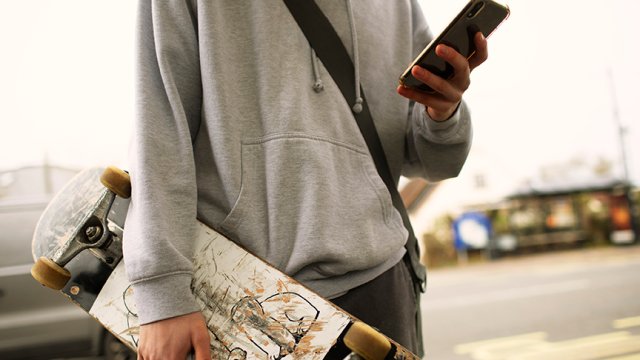 ung gutt med mobiltelefon og skateboard.