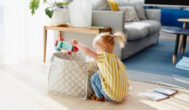 Liten jente sitter på gulvet og henter fram leker fra en lekekasse