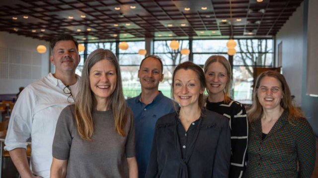 To menn og fire kvinner i et prosjektteam som står på rad og smiler mot kamera