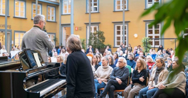 En stor gruppe mennesker sitter og ser opp på en person som taler fra scenen