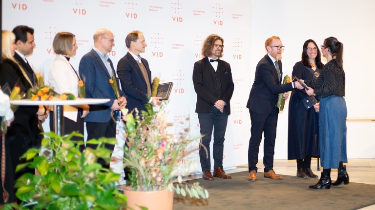 en rekke mennesker stående på scenen, en person håndhilser på en annen av dem. 