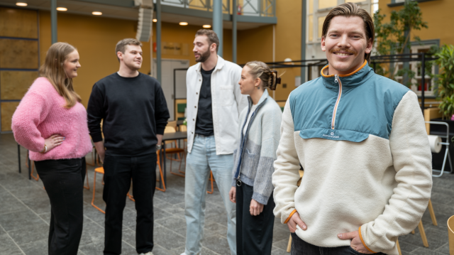 En mannlig student i forgrunn med fire studenter stående litt i bakgrunn.
