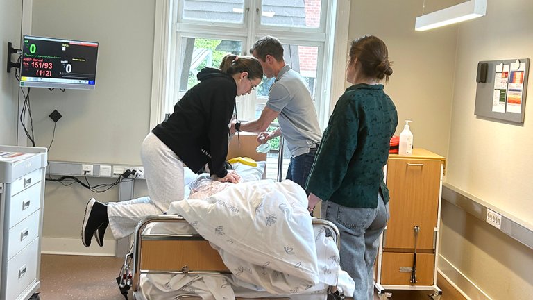 en student gjør HRL på en dukke i seng mens to andre studenter står ved siden av og ser på. 