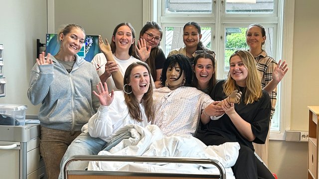 Studenter står samlet rundt en sykehusseng og smiler til kamera.