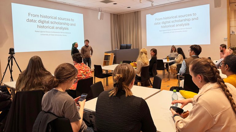 Studentene sitter i undervisningsrom med powerpointpresentasjon på veggen