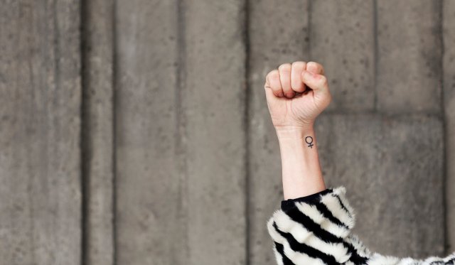 knyttet kvinnehånd med kvinnesymbol tatovert på håndleddet strekkes i været